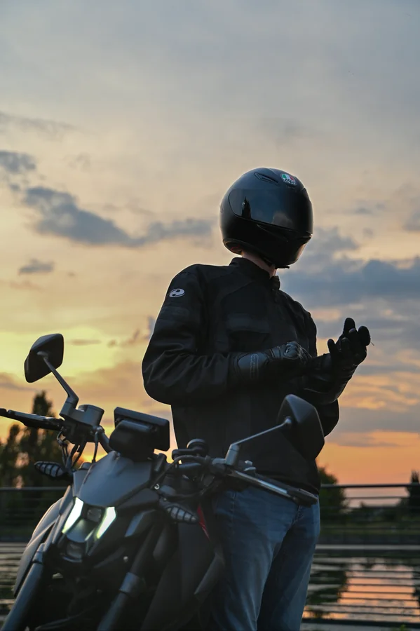 Un motociclista con casco e guanti in sella a una moto davanti al cielo del tramonto.