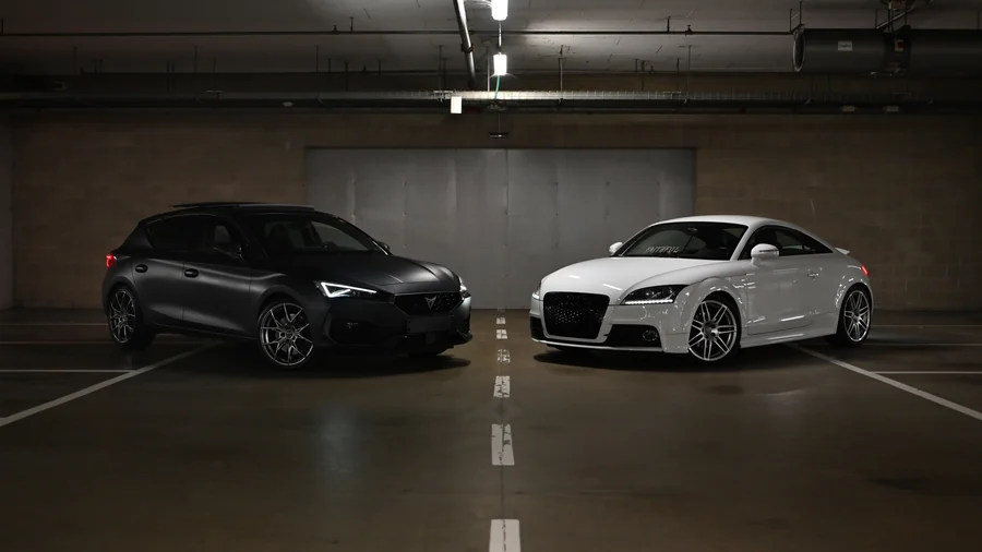 Due auto sportive, una scura e una bianca, in un parcheggio sotterraneo.